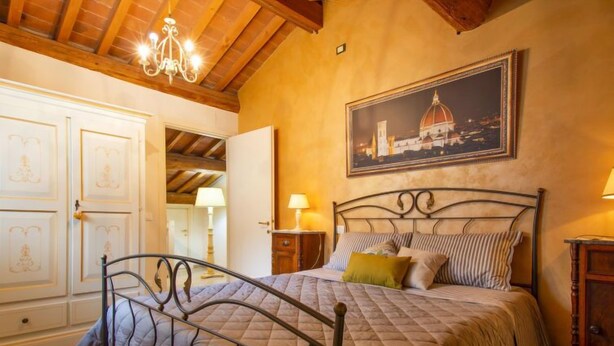 Une chambre à coucher avec un lit, un lustre, un tableau représentant un bâtiment et un plafond en bois.