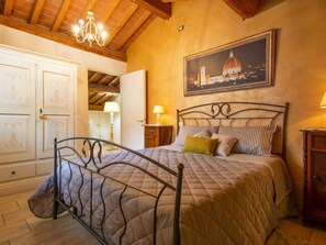 Un dormitorio con cama, candelabro, un cuadro de un edificio y techo de madera.