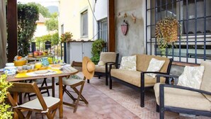 Une terrasse extérieure avec une table ronde en bois, des chaises et un canapé. On y trouve également des plantes en pot et une lanterne suspendue.