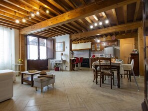 Amplia sala de estar con techo de madera, mesa de comedor con sillas, cocina con electrodomésticos modernos y un gran ventanal que proporciona luz natural.
