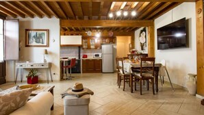 Un salon confortable avec un canapé, un pouf et un chapeau posé sur le pouf. On y trouve également un coin repas avec des chaises et une table en bois. La cuisine est équipée de meubles en bois, d’un réfrigérateur et d’un four à micro-ondes.