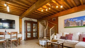 Un vaste salon doté d’un plafond en bois, un coin repas avec une grande télévision et un escalier menant à un autre niveau.