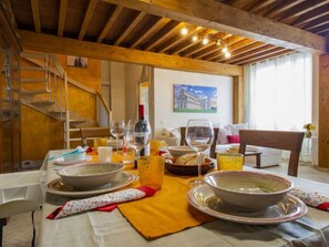 A dining area with a table set for a meal, featuring a painting on the wall and a window with curtains.
