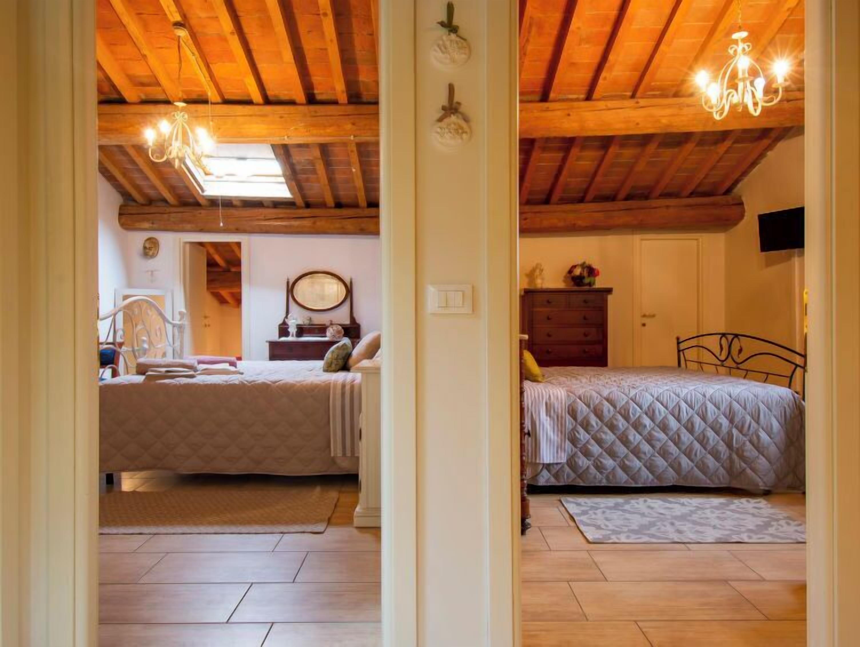 Een slaapkamer met twee bedden, houten balken in het plafond, een kroonluchter en een dressoir.