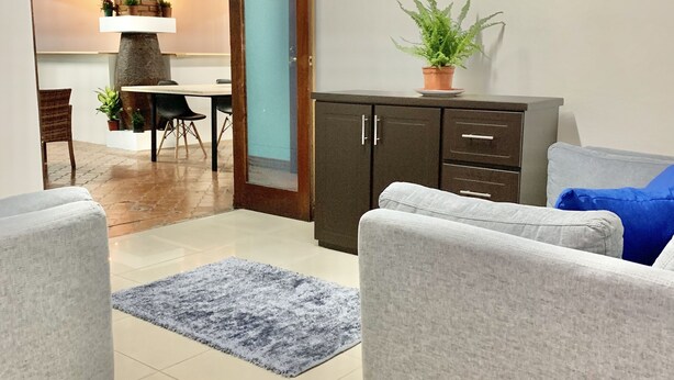 A modern living room with a grey sofa, a blue rug, and a wooden cabinet. - Global House Costa Rica Backpackers (Alajuela)