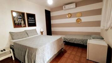 Un dormitorio con una cama grande, una cama más pequeña, una mesita de noche, una lámpara y un aire acondicionado de pared.