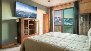 A bedroom with a large bed, a television on the wall, and a balcony with a view. - Sky Ridge. Movie Room. Games. Views. Spa. BBQ. (Big Bear Lake)