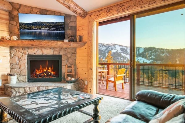 A cozy room with a stone fireplace, a flat-screen TV mounted above it, and a glass table.