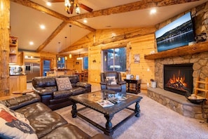 A log cabin interior with a living room, fireplace, kitchen, and dining area.