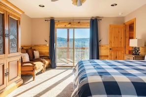 Un dormitorio con una cama grande, un armario de madera, una zona de estar con sofá y sillón, y un balcón con vistas.