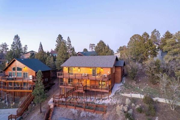 Una cabaña de madera de varios pisos con balcones, una terraza y un paisaje natural circundante.