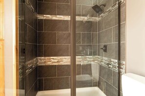Una ducha con azulejos oscuros y puerta de cristal.
