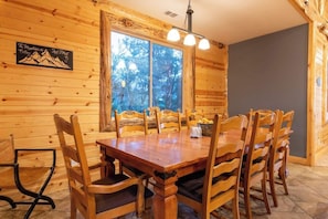 A wooden interior with a dining table and chairs, a large window with a view of trees, and a sign on the wall.