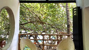 Una habitación con techo alto, un ventanal grande, dos sillones de mimbre, una mesita con un cuenco de flores y suelo de madera.