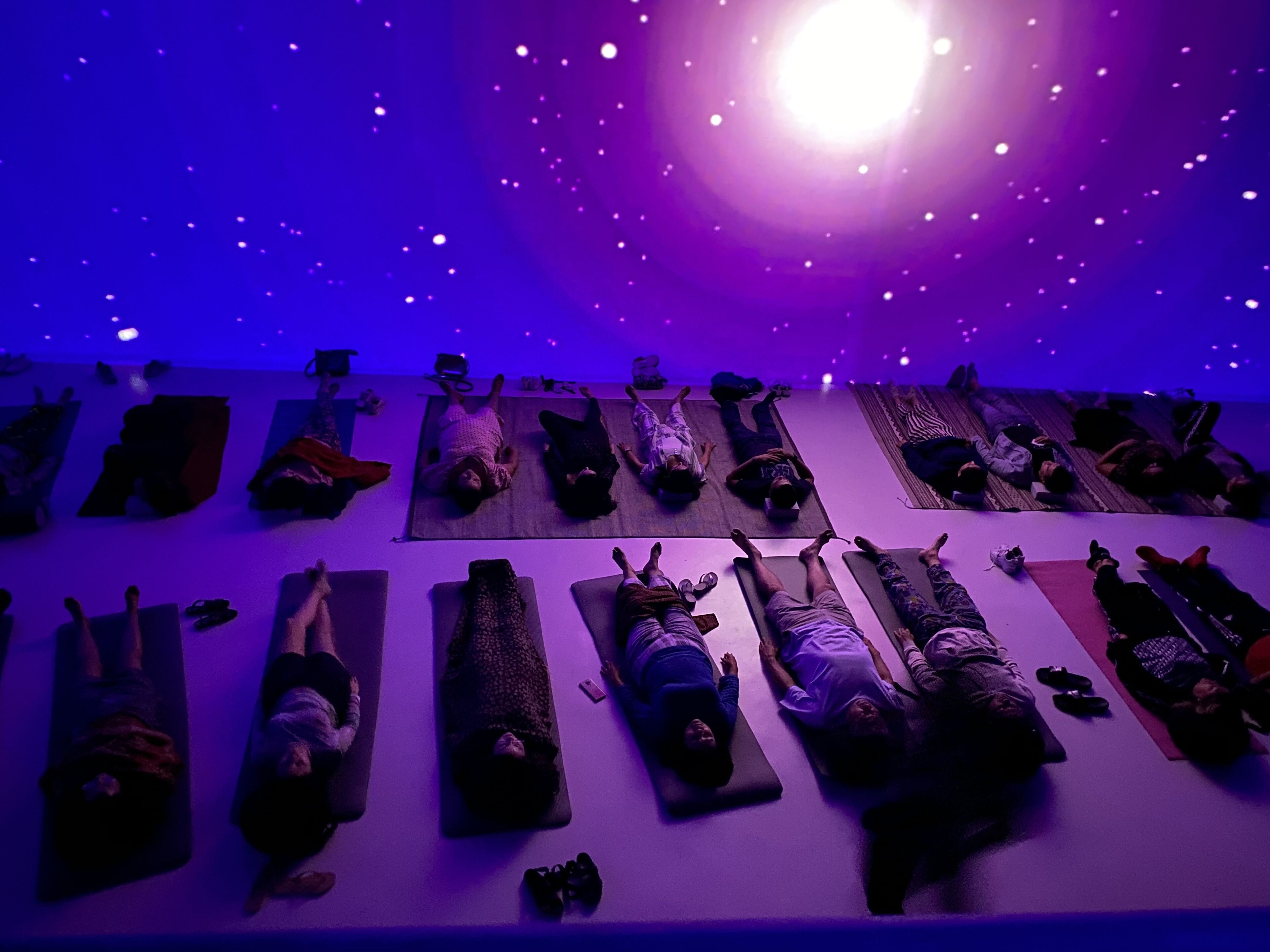 A yoga class with participants lying on mats in a dimly lit room with a starry ceiling.