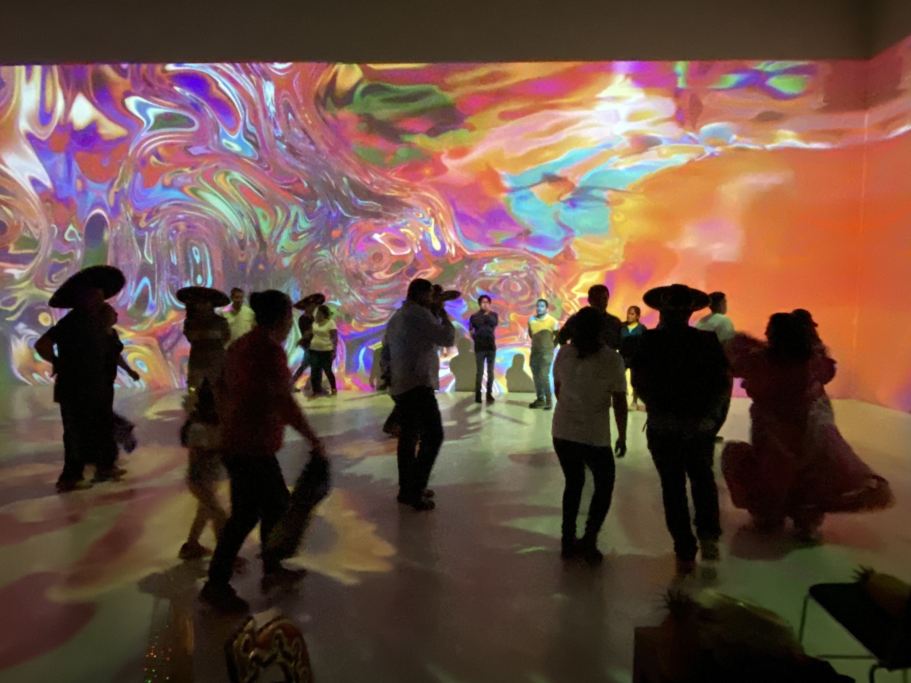 Un grupo de personas en una habitación con una llamativa exhibición de luces abstractas en la pared.