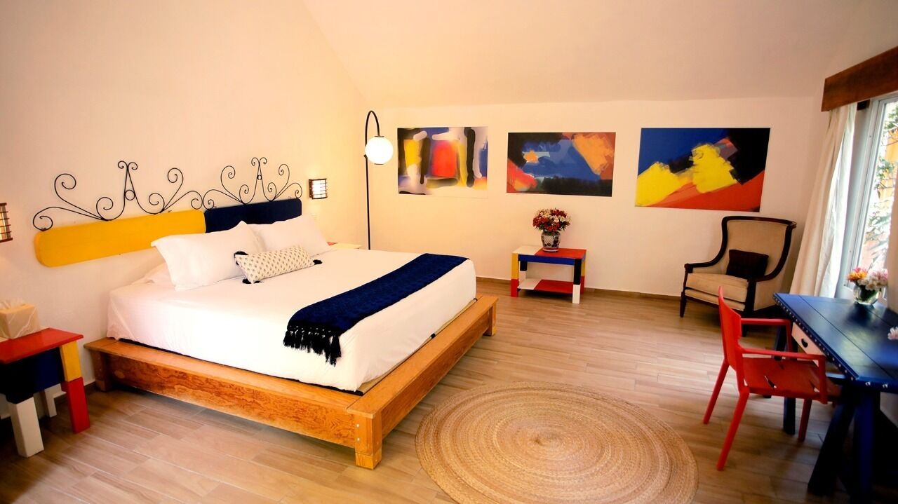 Un dormitorio con una cama de madera, un escritorio, una silla y obras de arte en las paredes.