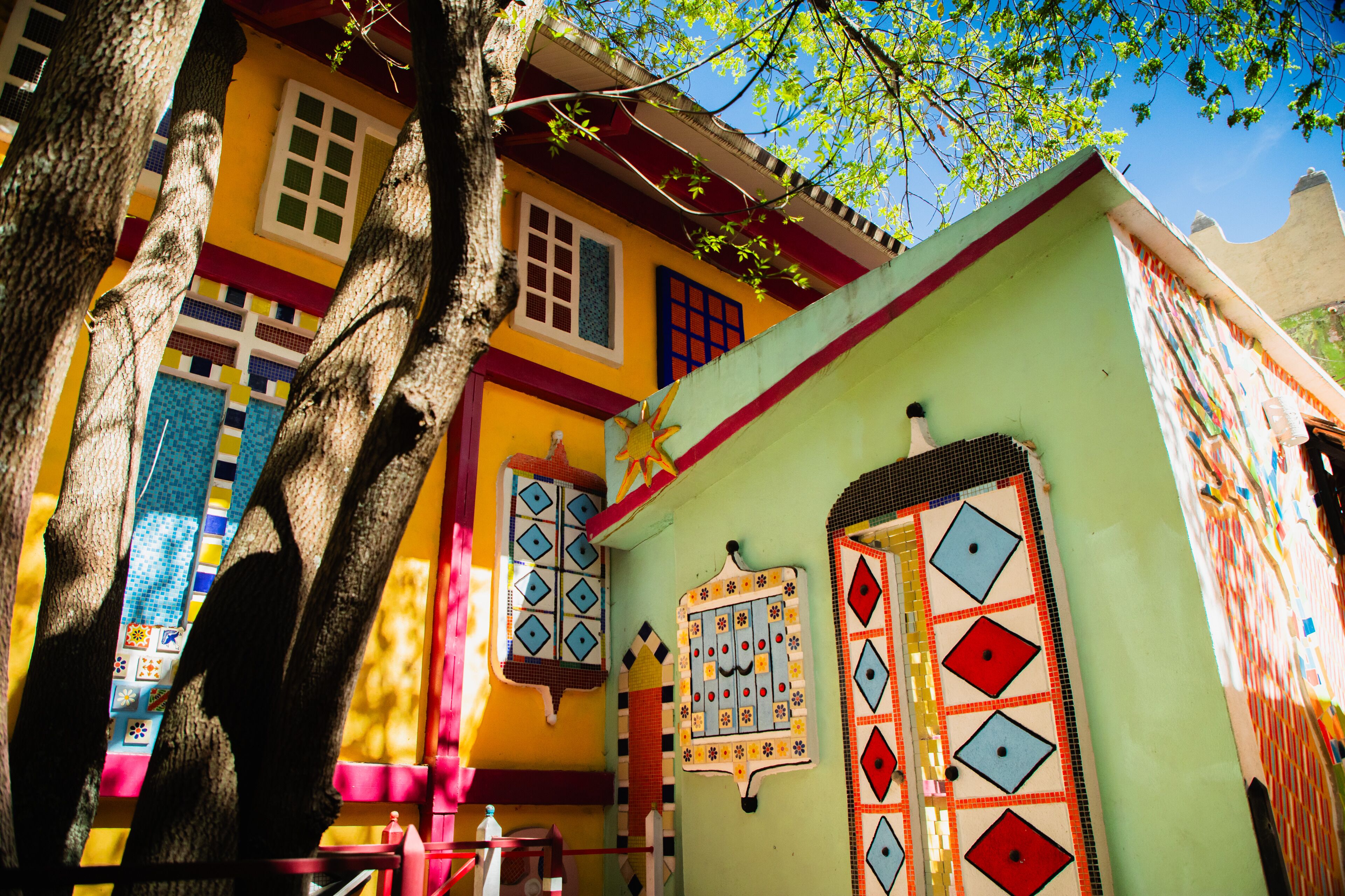 Un edificio colorido con fachada verde, puerta roja y ventana con diseño azul y blanco.