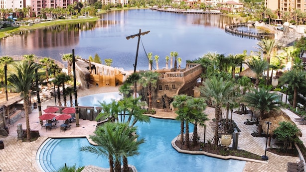 A resort with a large central pool, palm trees, and a castle-like structure.