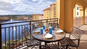 A balcony with a table set for two, overlooking a body of water and a cityscape.