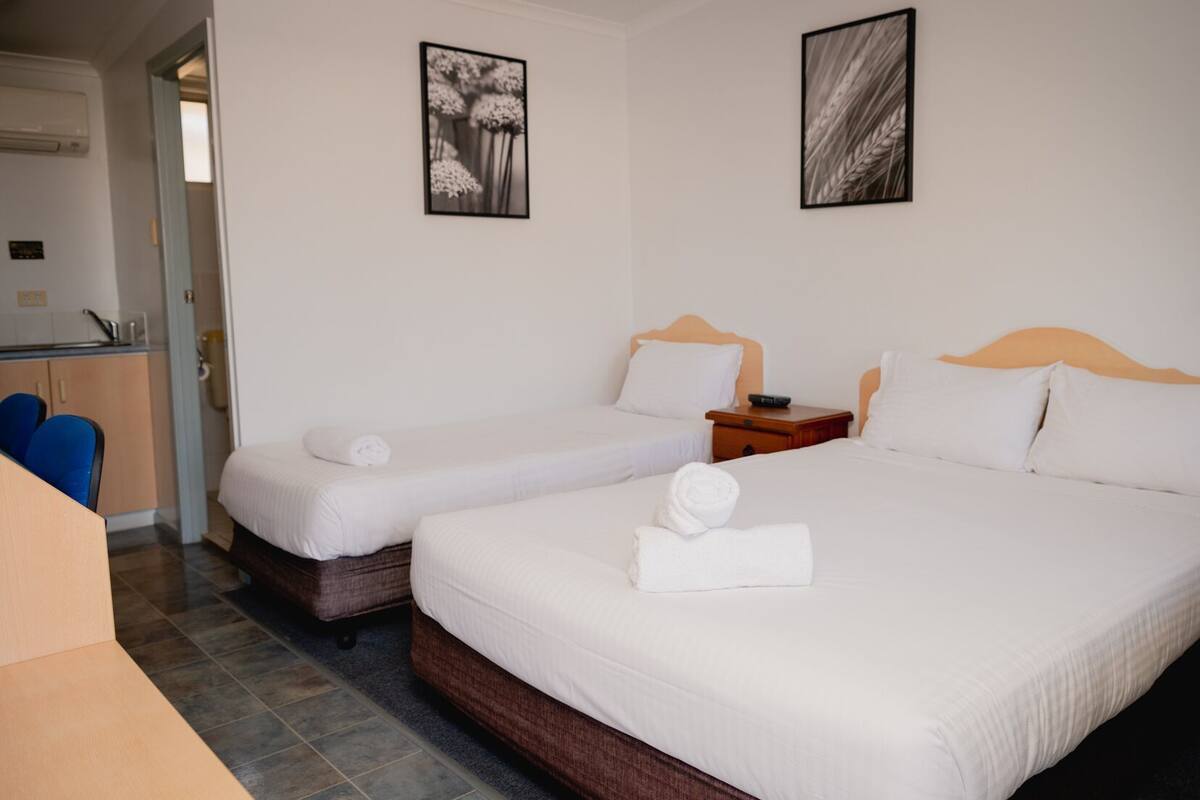 Een hotelkamer met twee enkele bedden, een houten hoofdbord, een klein nachtkastje en een stoel.