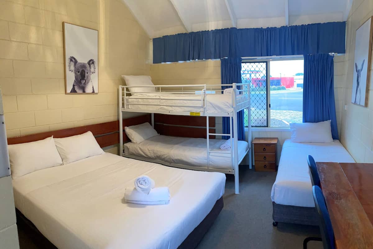 Een slaapkamer met een stapelbed, twee eenpersoonsbedden, een houten tafel en een raam met gordijnen.