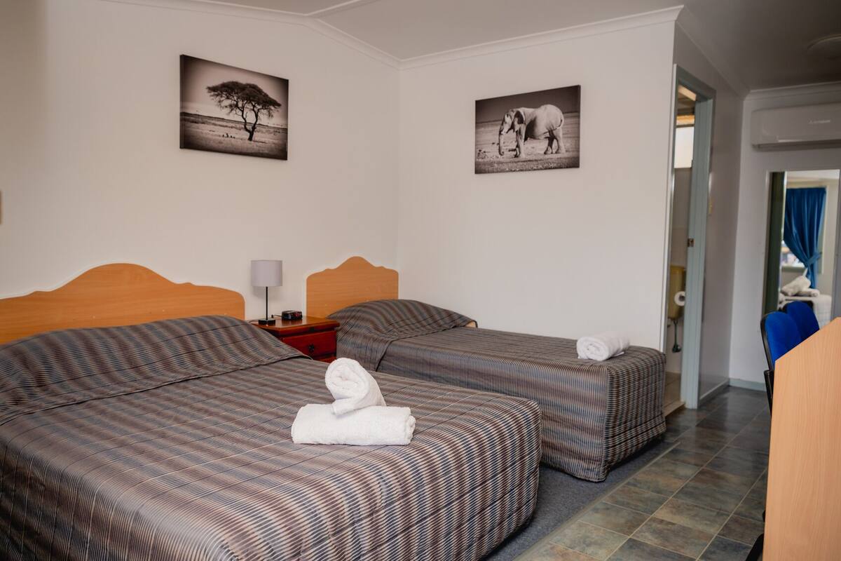 Een hotelkamer met twee bedden, een nachtkastje, een lamp en twee aan de muur hangende foto's.
