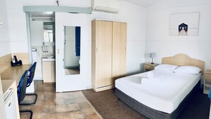 Ein Hotelzimmer mit Bett, Schreibtisch mit Stuhl, Kleiderschrank und einem durchgegangenen Tür sichtbaren Badezimmer.