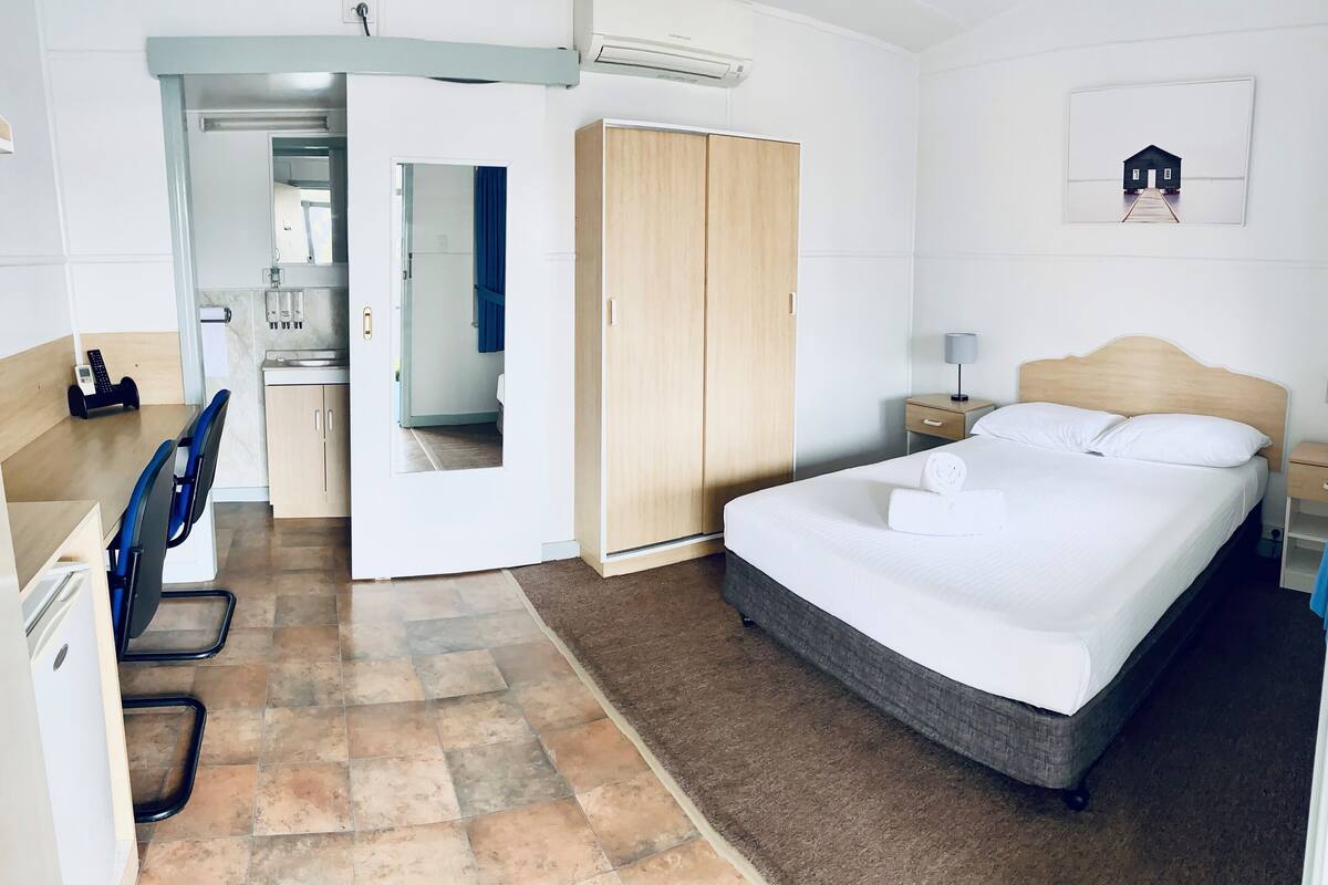 Hotelkamer met een bed, een bureau met stoel, een kledingkast en een badkamer zichtbaar door een geopende deur.
