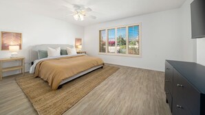A bedroom with a bed, bedside tables, a ceiling fan, a TV, and a window with blinds. - Stylish 3 bedroom condo w/ office & 3 pools (Palm Desert)