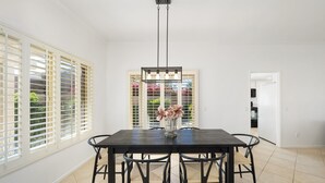 A dining area with a dark wooden table, six chairs, and a vase with flowers. - Stylish 3 bedroom condo w/ office & 3 pools (Palm Desert)