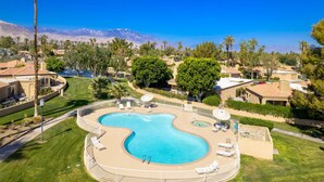 A resort with a large, curved swimming pool surrounded by lounge chairs and umbrellas, set against a backdrop of palm trees and mountains. - Stylish 3 bedroom condo w/ office & 3 pools (Palm Desert)