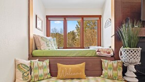 A cozy seating area with a bench and cushions, a window with a view of trees, and a decorative plant. - RMR: Hawthorne 222 Condo in The Aspens/Wilson,WY (Wilson)
