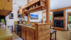 A rustic kitchen with wooden cabinetry, a built-in microwave, and a stone fireplace. - RMR: Hawthorne 222 Condo in The Aspens/Wilson,WY (Wilson)