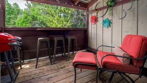 A covered patio area with wooden flooring, a red grill, and three bar stools. - RMR: Hawthorne 222 Condo in The Aspens/Wilson,WY (Wilson)