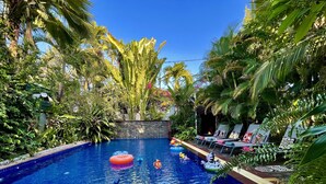Ein Swimmingpool, umgeben von üppiger Vegetation, mit Liegestühlen und einer dekorativen Wand.