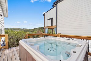 A hot tub on a wooden deck with a view of a hillside.