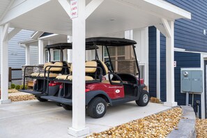 A golf cart parked under a covered area with a house in the background.