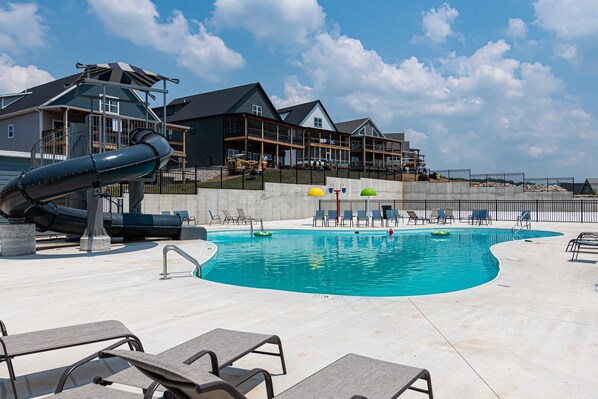 A swimming pool with a slide, lounge chairs, and a building with balconies in the background.