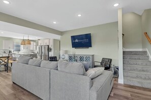A modern living room with a grey sectional sofa, a dining area with a wooden table, and a kitchen with white cabinets and a built-in oven. - Enjoy a Private Pool with Panoramic Views, Elevator Access, Private Golf Cart & Free Tickets! (Hollister)