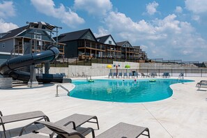 A swimming pool with lounge chairs and a slide, surrounded by a building with multiple balconies.