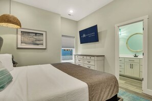 A bedroom with a bed, a dresser, a mirror, a framed picture, and a television on the wall.