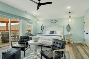 A bedroom with a bed, two chairs, a table, and a ceiling fan.