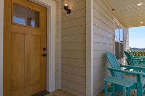 A wooden door with a window, a porch with teal Adirondack chairs, and a light fixture on the wall.