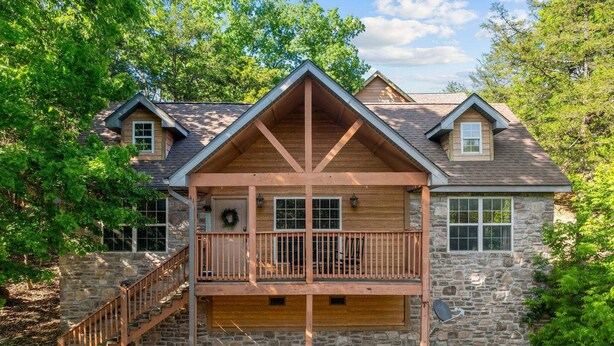 A two-story log cabin with a stone foundation, a wooden balcony, and a stone chimney.