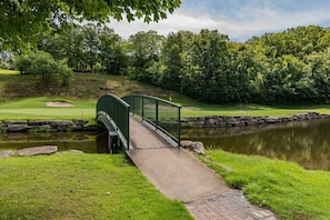 A green bridge over a pond with a golf course in the background.