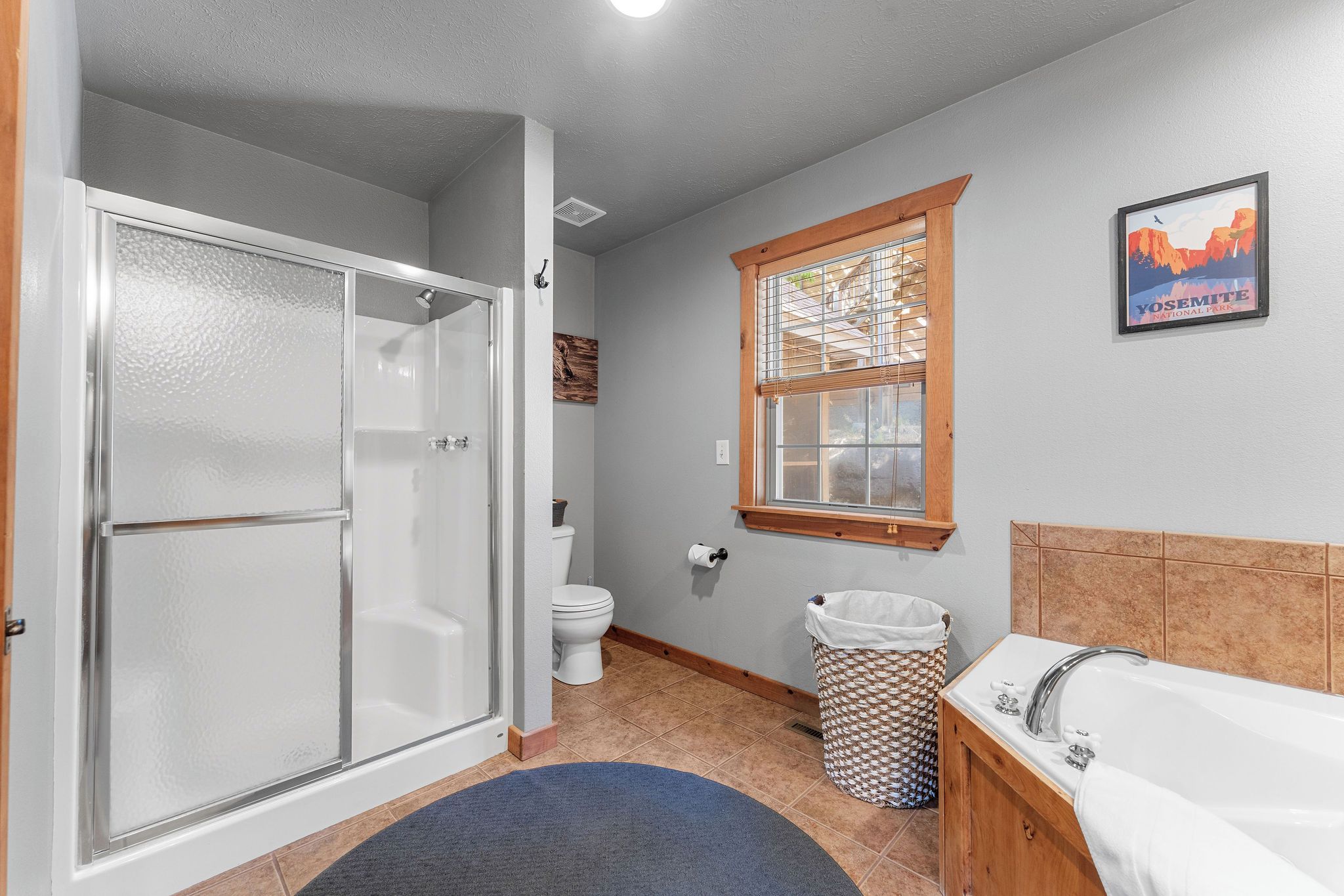 Une salle de bain dotée d’une douche à parois de verre, de toilettes, d’une fenêtre donnant sur le parc national de Yosemite et d’une baignoire.
