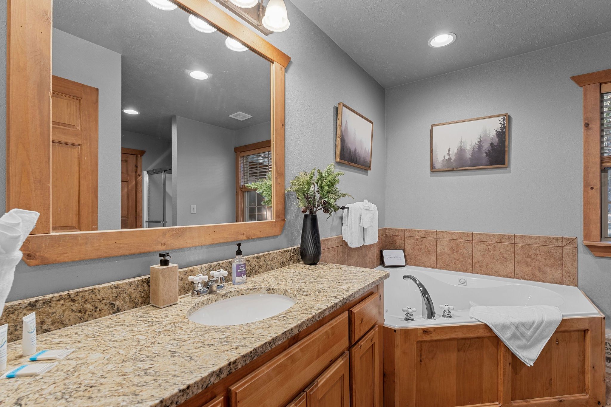 A bathroom with a large mirror, a sink, a bathtub, wooden cabinets, and a framed picture on the wall.