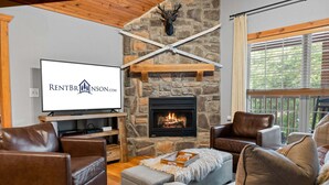 A living room with a stone fireplace, a television, leather sofas, and a wooden ceiling.