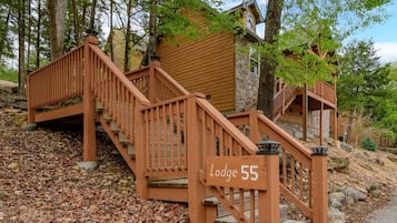 A wooden staircase leading to a lodge with a stone exterior, surrounded by trees.